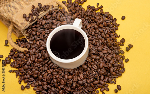 Cup of coffee beans and burlap sack on yellow background, copy space banner