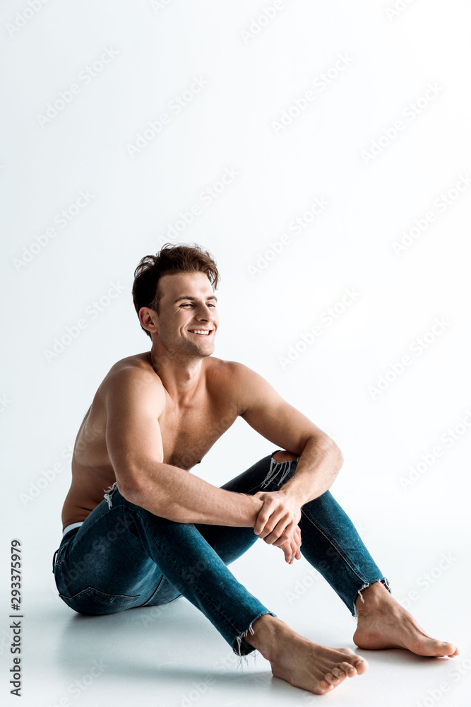 Obraz premium cheerful shirtless man with barefoot sitting on white