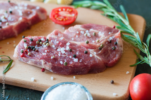 Piece of raw pork meat sprinkled with pepper and salt with chopped tomato and rosemary, process of cooking steak