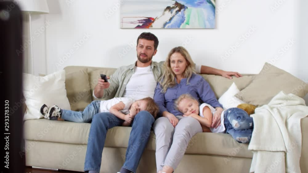 Handheld shot of bearded man and beautiful woman sitting on sofa and watching TV as little children sleeping on their lapsHandheld shot of bearded man and beautiful woman sitting on sofa and watching Handheld shot of bearded man and beautiful woman sitting on sofa and watching TV as little children sleeping on their lapsHandheld shot of bearded man and beautiful woman sitting on sofa and watching
