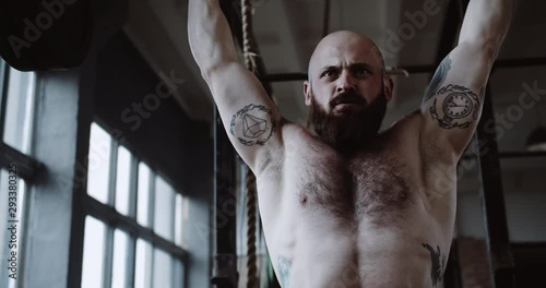Close-up young Caucasian athlete man lifting heavy barbell in large hardcore gym hall. Ambition and challenge concept.