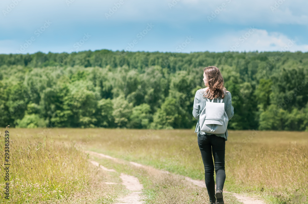 Young lonely girl walks a country road towards a dense forest Young lonely girl walks a country road towards a dense forest