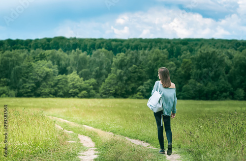 Young lonely girl walks a country road towards a dense forest