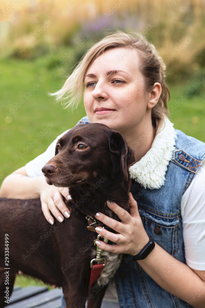 Portrait of a young woman with a dog. Woman with blond hair hugs a brown dog for a walk in a city park. Portrait of a young woman with a dog. Woman with blond hair hugs a brown dog for a walk in a city park.