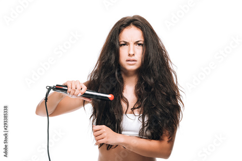 stressed brunette beautiful woman styling curly hair with flat iron isolated on white