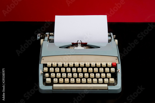 Manual typewriter with blank white paper on red and black background