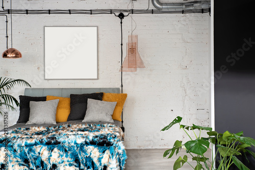 Interior of bedroom in loft apartment with double bed with pillows and gold and modern lamps. Brick wall with frame with mock up. Industrial and scandinavian style.