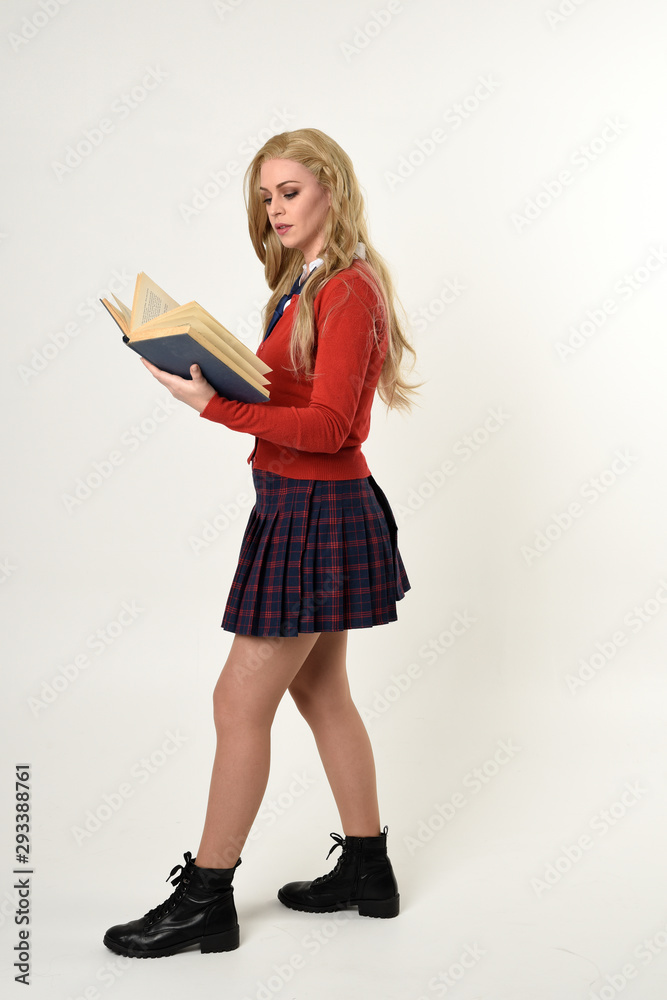 full length portrait of blonde girl wearing red cardigan with tie and plaid skirt, school uniform, standing pose holding books, facing the camera, on a white studio background. full length portrait of blonde girl wearing red cardigan with tie and plaid skirt, school uniform, standing pose holding books, facing the camera, on a white studio background.