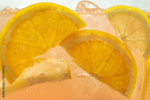 Close up of lemon slices in lemonade and ice cubes background. Texture of cooling sweet summer's drink with macro bubbles on the glass wall. Fizzing or floating up to top of surface.