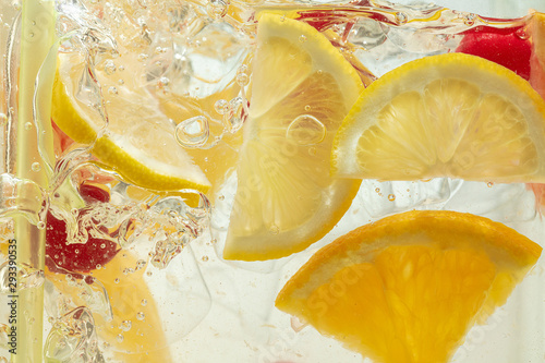 Close up of lemon slices and cherry in lemonade and ice cubes background. Texture of cooling sweet summer's drink with macro bubbles on the glass wall. Fizzing or floating up to top of surface.