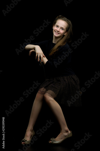 Charming girl teenager sitting on a chair in the studio on a bla