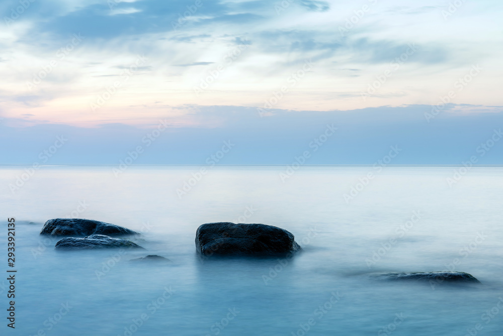 long exposure smooth sea surface with large stones sticking out of the water in blue twilight