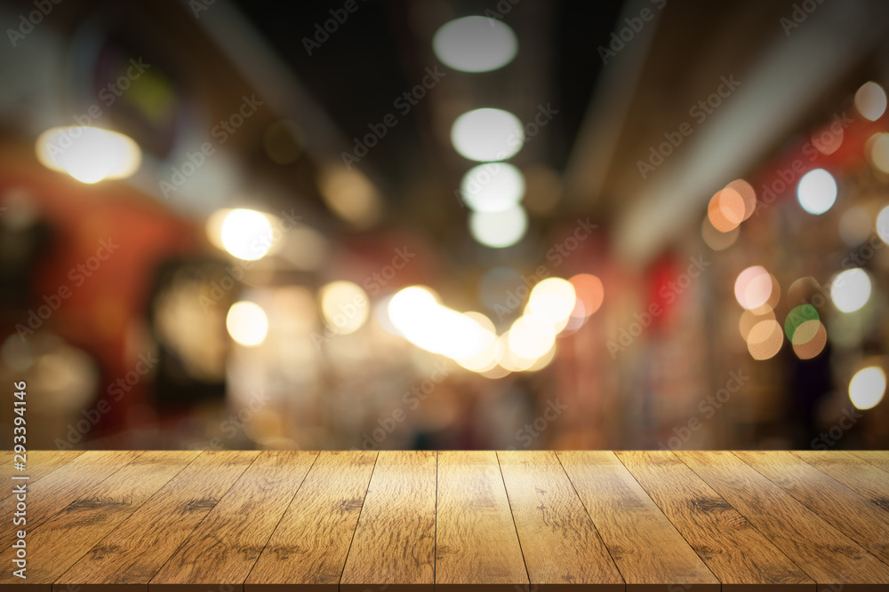 Empty wooden table in front with blurred background of night market.