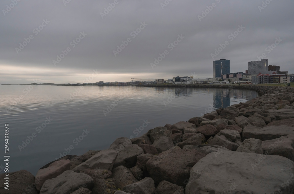 Seascape with stone coast in reykjavik, iceland. City building on sea side. Skyline on cloudy sky. Architecture and construction. Early morning, mooody sky.