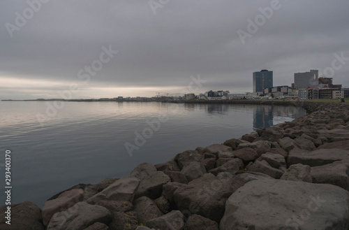 Seascape with stone coast in reykjavik  iceland. City building on sea side. Skyline on cloudy sky. Architecture and construction. Early morning  mooody sky.