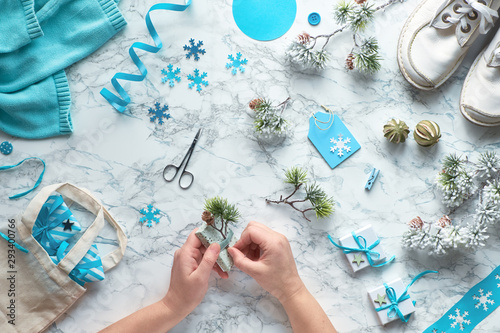 Wintertime, creative flat lay with various winter craft supplies, christmas tree twigs and hands decorating gift boxes
