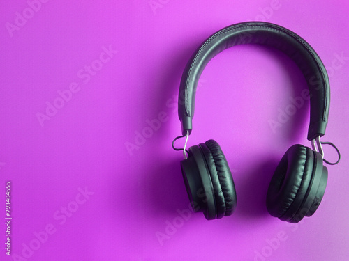Wireless black headphones on purple background with copy space. Music concept. Flat lay, top view.