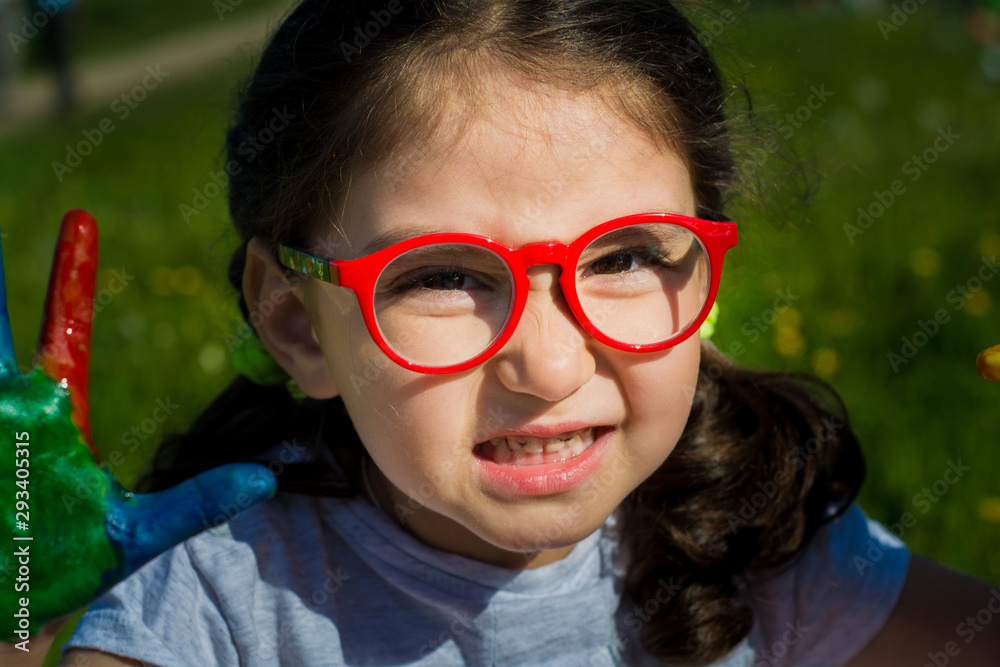 Summer. Open space. The girl held out her hands. Hands painted with colored paint. The girl is wearing glasses. Summer. Open space. The girl held out her hands. Hands painted with colored paint. The girl is wearing glasses.