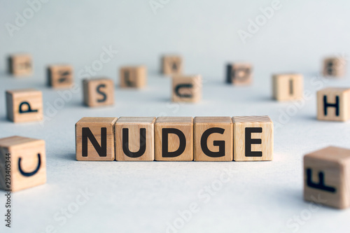 Nudge - word from wooden blocks with letters, pushing gently concept, random letters around, white  background photo