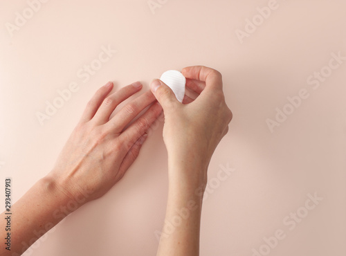 Female hands washes from nails with cotton pad on pink background