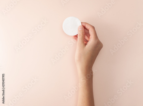 Cotton pad in the female right hand on a pink background