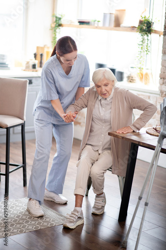 Nurse assisting aged woman in making steps after surgery