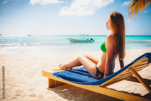 Holiday vacation beach - beautiful young girl relaxing on lounger on paradise caribbean beach with white sand and palms near blue sea on warm summer day © Vasily Makarov