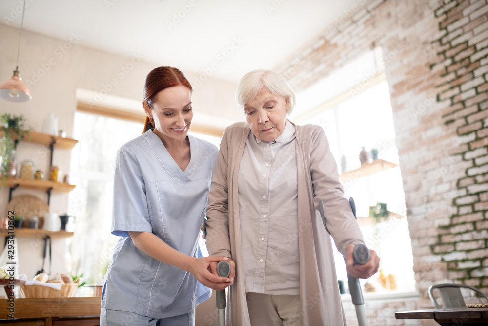 Fototapeta premium Pensioner walking with crutches standing near caregiver