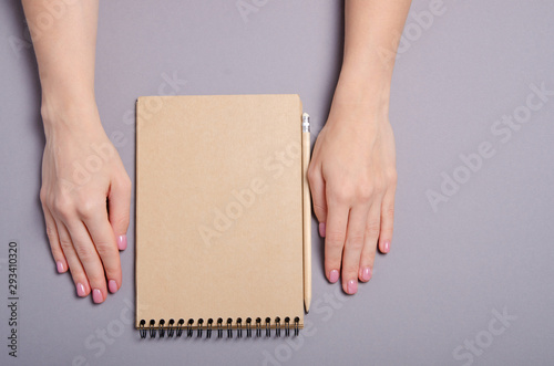 Brown notebook empty with pencil in hand on gray background, top view © Kabardins photo