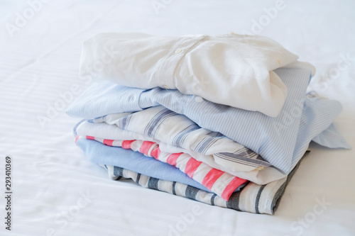 Hotel room with freshly made bed, perfectly clean and ironed sheets, stack of new dry cleaned folded set of clothing in natural sun light. Close up, copy space for text.