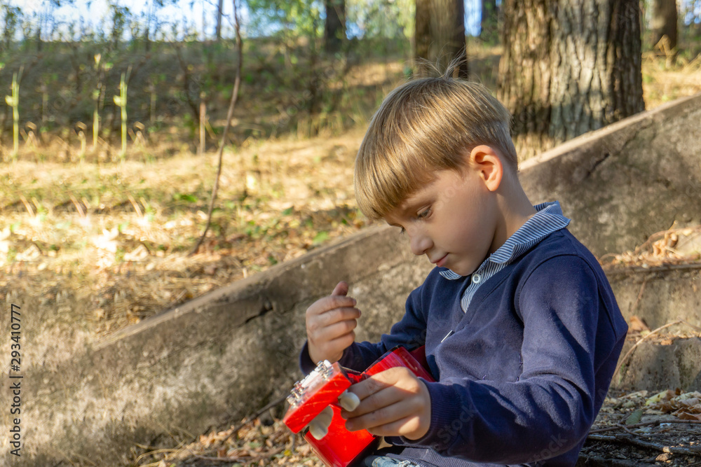 A boy in a blue jacket and jeans plays the guitar on the old steps in an abandoned park.