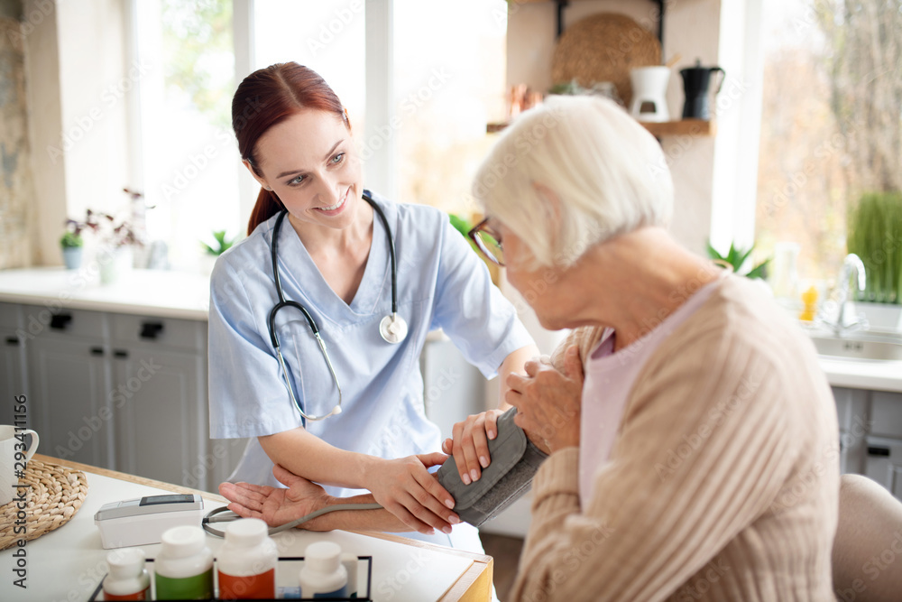 Obraz premium Nurse wearing uniform measuring blood pressure for pensioner