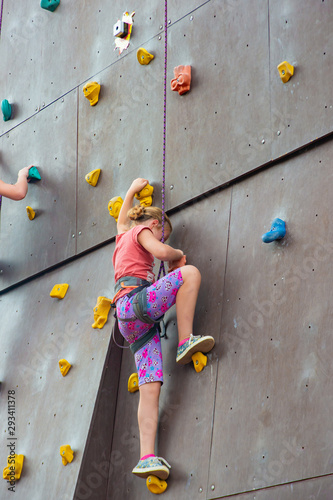 A girl creeps up on an artificial rock-climbing tower with insurance in an extreme sports park.