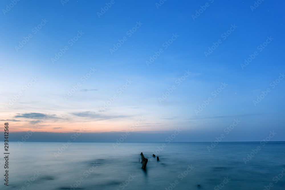 long exposure smooth sea surface with breakwater sticking out of the water in blue twilight
