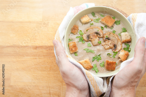 A man puts hot mushroom cream soup with croutons and parsley. Top view of a hot dish.