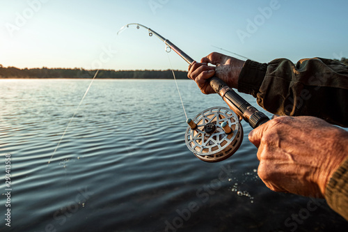Canvas Hands of a man in a Urp plan hold a fishing rod, a fisherman catches fish at dawn