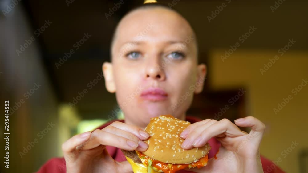 bald girl in a cafe eating a hamburger. close-up. looking at the camera bald girl in a cafe eating a hamburger. close-up. looking at the camera