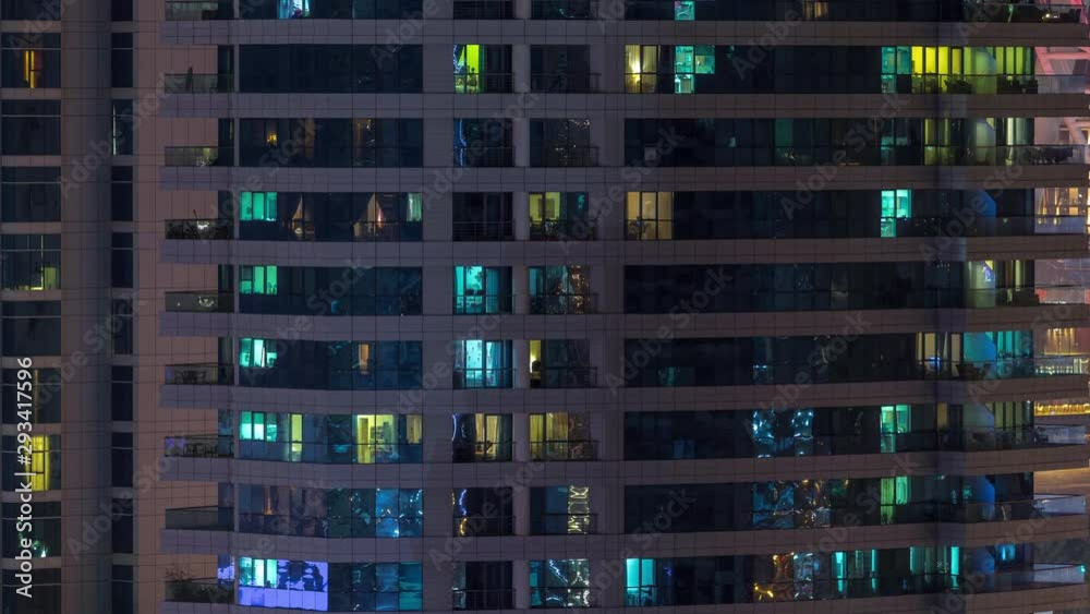 Rows of glowing windows with people in the interior of apartment building at night. Modern skyscraper with glass surface. Concept for business and modern life. Tilt up Rows of glowing windows with people in the interior of apartment building at night. Modern skyscraper with glass surface. Concept for business and modern life. Tilt up