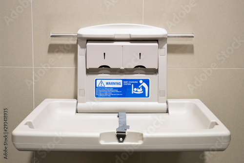 Fototapeta Naklejka Na Ścianę i Meble -  Baby changing station in a public restroom. white plastic diaper table on brown tile wall in toilet.