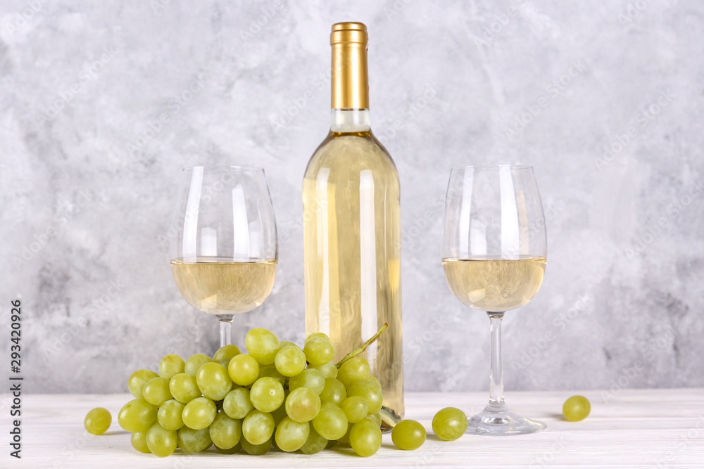 Obraz premium Vintage bottle of white wine without label, two glasses and bunch of grapes on wooden table, lofty grunged concrete wall background. Expensive bottle of chardonnay concept. concept. Copy space,
