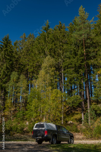 Big blue off-road car with white roof in color autumn forest in mountains Sumava