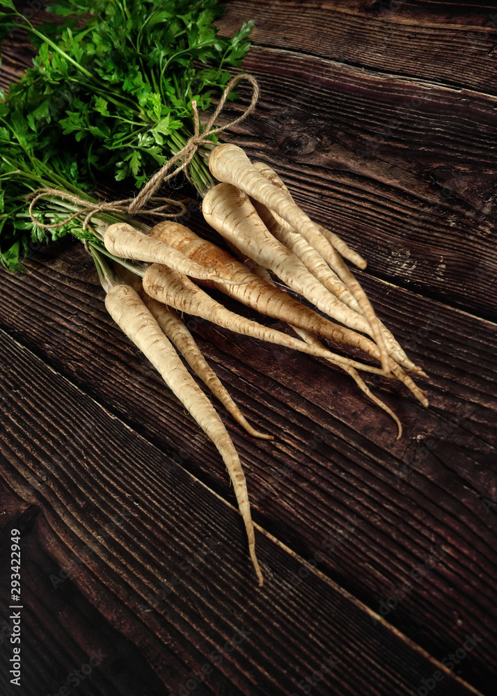 Bunch of parsnips with green leaves on dark wooden desk.