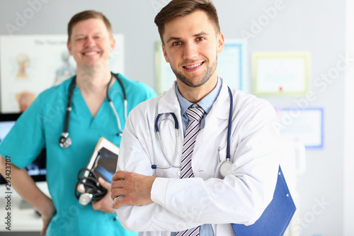 Portrait of handsome man doc with stethoscope. Smiling physician posing in clinic cabinet with arms crossed. Medical treatment concept. Blurred background