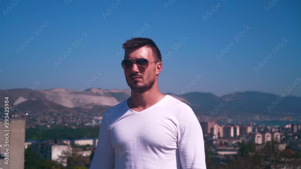 Young attractive man in glasses and a white longsleeve against the backdrop of the city at altitude. Rear view, stunning panoramic views of the city, the bay of the sea and mountains from a height.