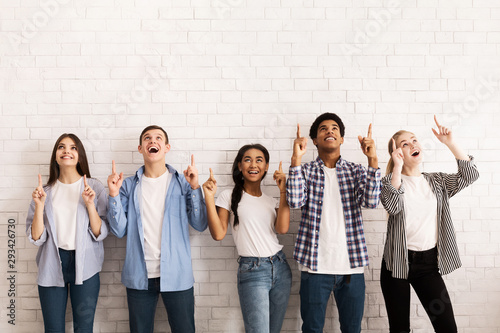 Teen friends pointing up on free space over white wall photo