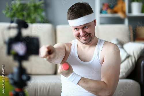 Happy Blogger with Dumbbell Training in Apartment. Smiling Sportsman Recording Video on Digital Camcorder for Sport Blog. Cheerful Man Doing Fitness Exercise at Home. Bearded Male Practice Aerobic © H_Ko