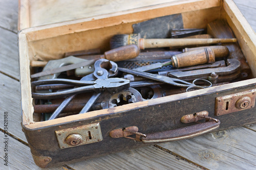 A suitcase with old hand tools on a wooden background. Focus on the suitcase