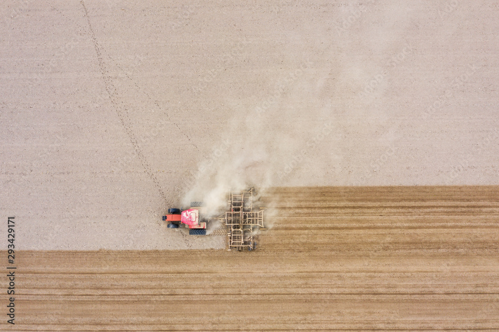 Fototapeta Tractor cultivates arable land with a disk harrow on an autumn day, view from a drone.