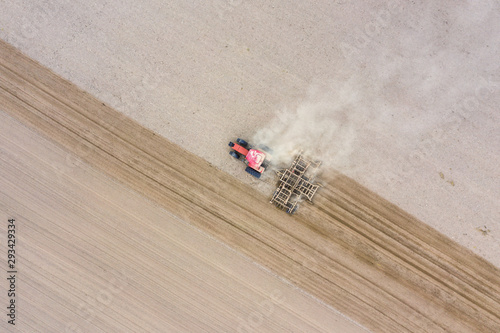 Tractor cultivates arable land with a disk harrow on an autumn day, view from a drone.