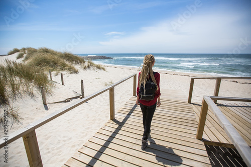 Young woman with blond dreadlocks standing near the ocean shore.